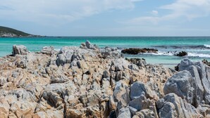 A rocky shoreline with large boulders and a clear view of the turquoise sea. - Romans Villa (Gansbaai)