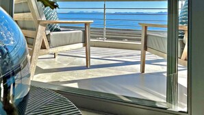 A balcony with a view of the sea, a glass door, and a plant. - Romans Villa (Gansbaai)