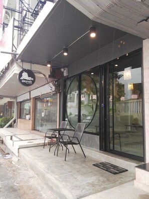 Una cafetería con terraza, un cartel y una escalera que sube a un nivel superior.
