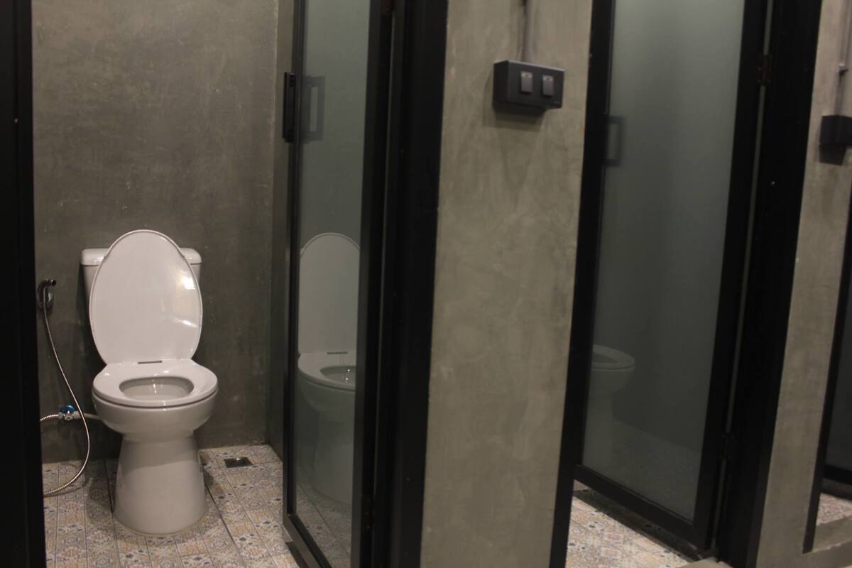 Baño público con inodoro, cabina de ducha y mampara de vidrio.