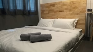 Ein ordentlich gemachtes Bett mit weißen Leinentüchern und zwei gefalteten grauen Handtüchern.