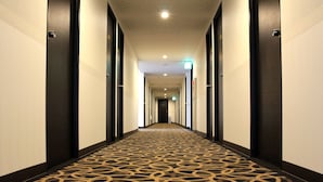 A hotel hallway with a patterned carpet, dark wooden doors, and a long corridor leading to a room. - Nagasaki Bus Terminal Hotel (Nagasaki)