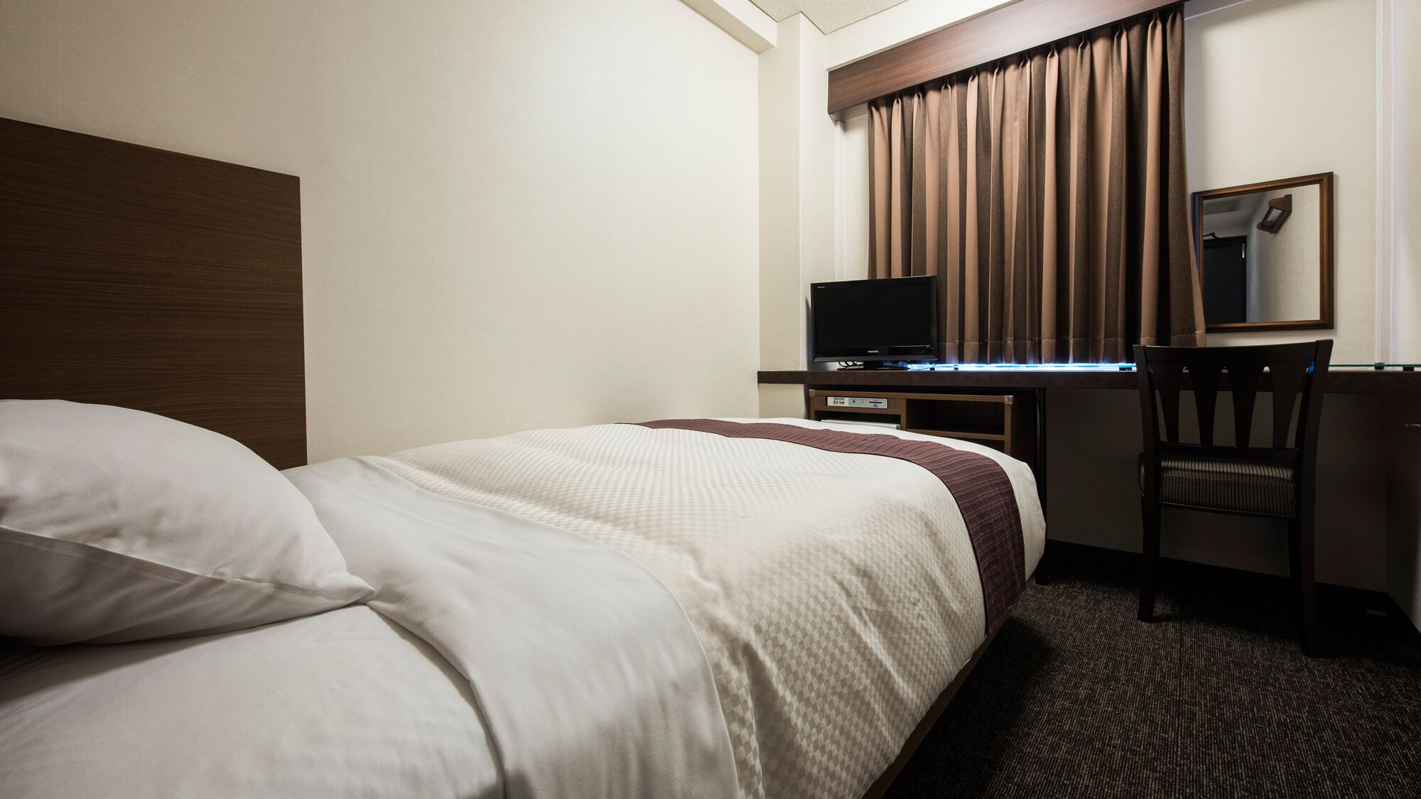 Une chambre d’hôtel comprenant un lit, un bureau avec une télévision, une chaise et un miroir.