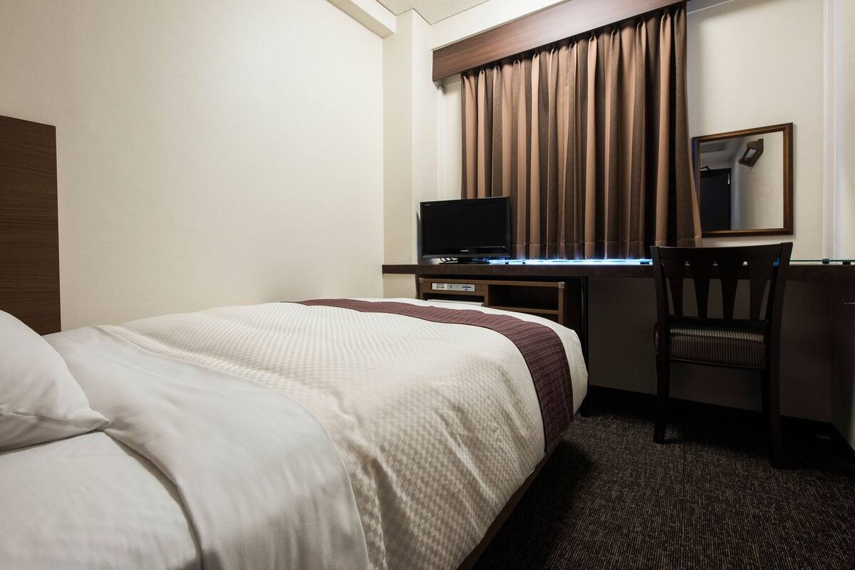 Une chambre d’hôtel comprenant un lit, un bureau avec une télévision, une chaise et un miroir.
