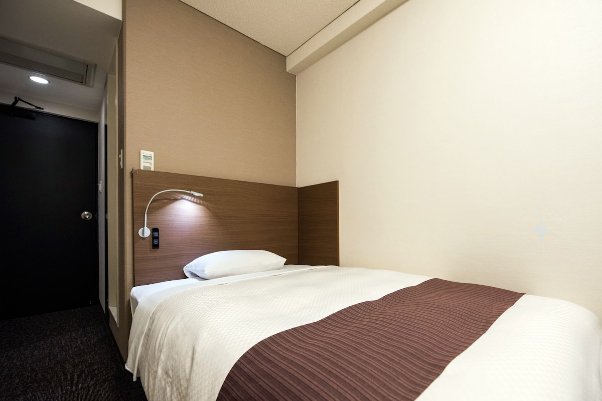 Une chambre d’hôtel avec un lit, une tête de lit, une lampe fixée au mur et une porte.