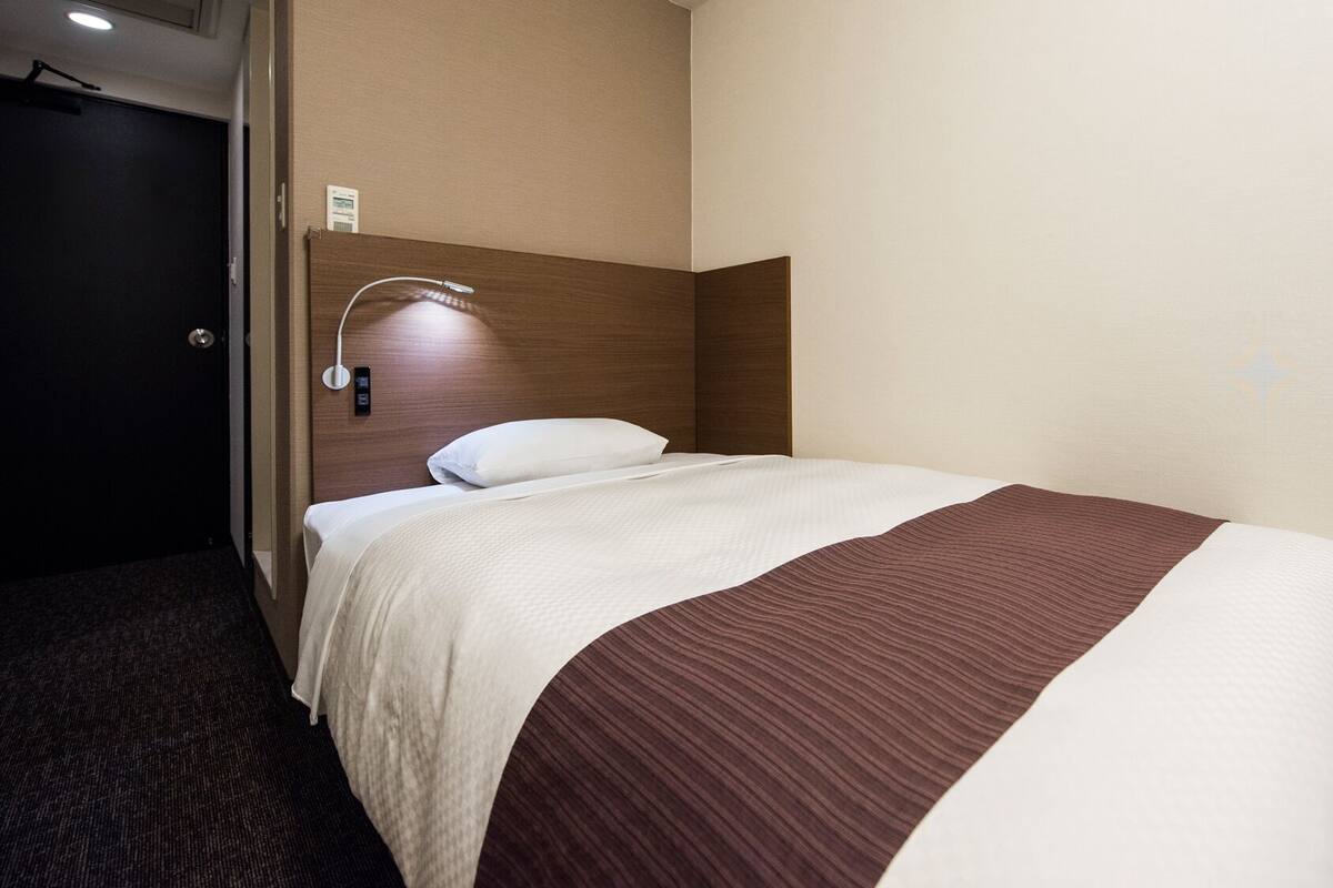 Une chambre d’hôtel avec un lit, une tête de lit, une lampe fixée au mur et une porte.