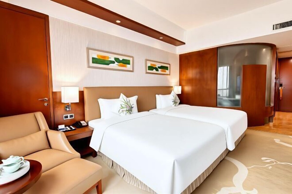 Ein Hotelzimmer mit einem großen Bett, einem Schreibtisch mit Stuhl, einem Nachttisch und einem an der Wand befestigten Telefon.