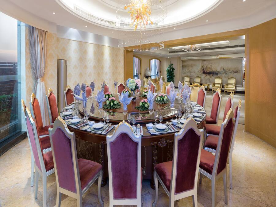 Une salle à manger élégante, avec une table ronde dressée pour le repas, entourée de chaises richement décorées.