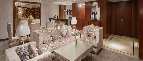 A spacious living area with a large sofa set, a coffee table, and a chandelier. There is a bar area with a mirror and decorative items.