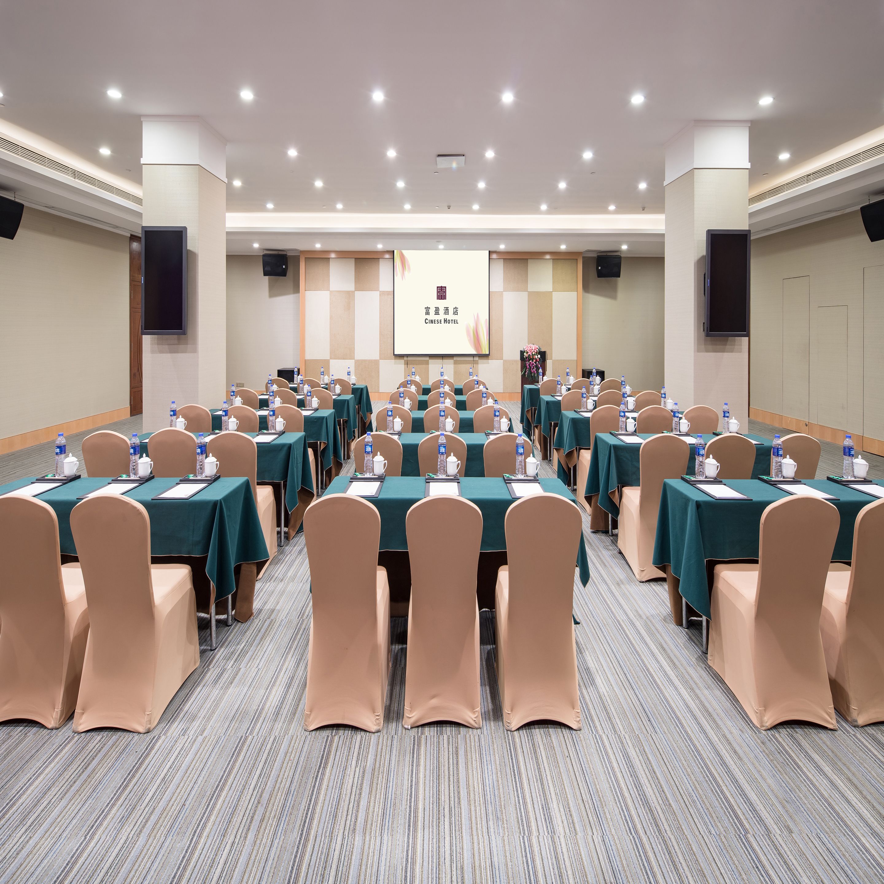 A conference room with multiple tables, chairs, and a presentation screen.