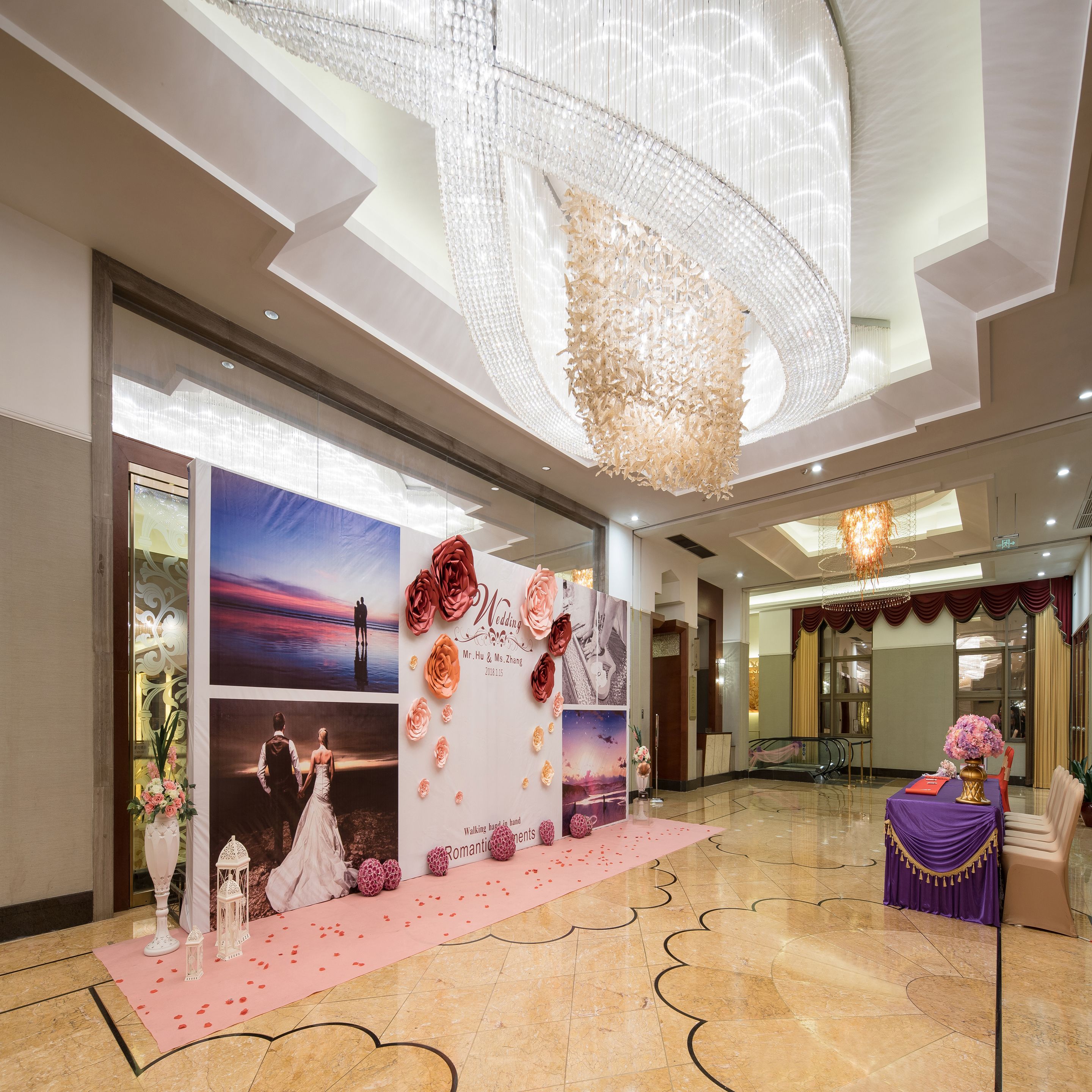 A spacious hotel lobby with a high ceiling, a large chandelier, and a reception desk.