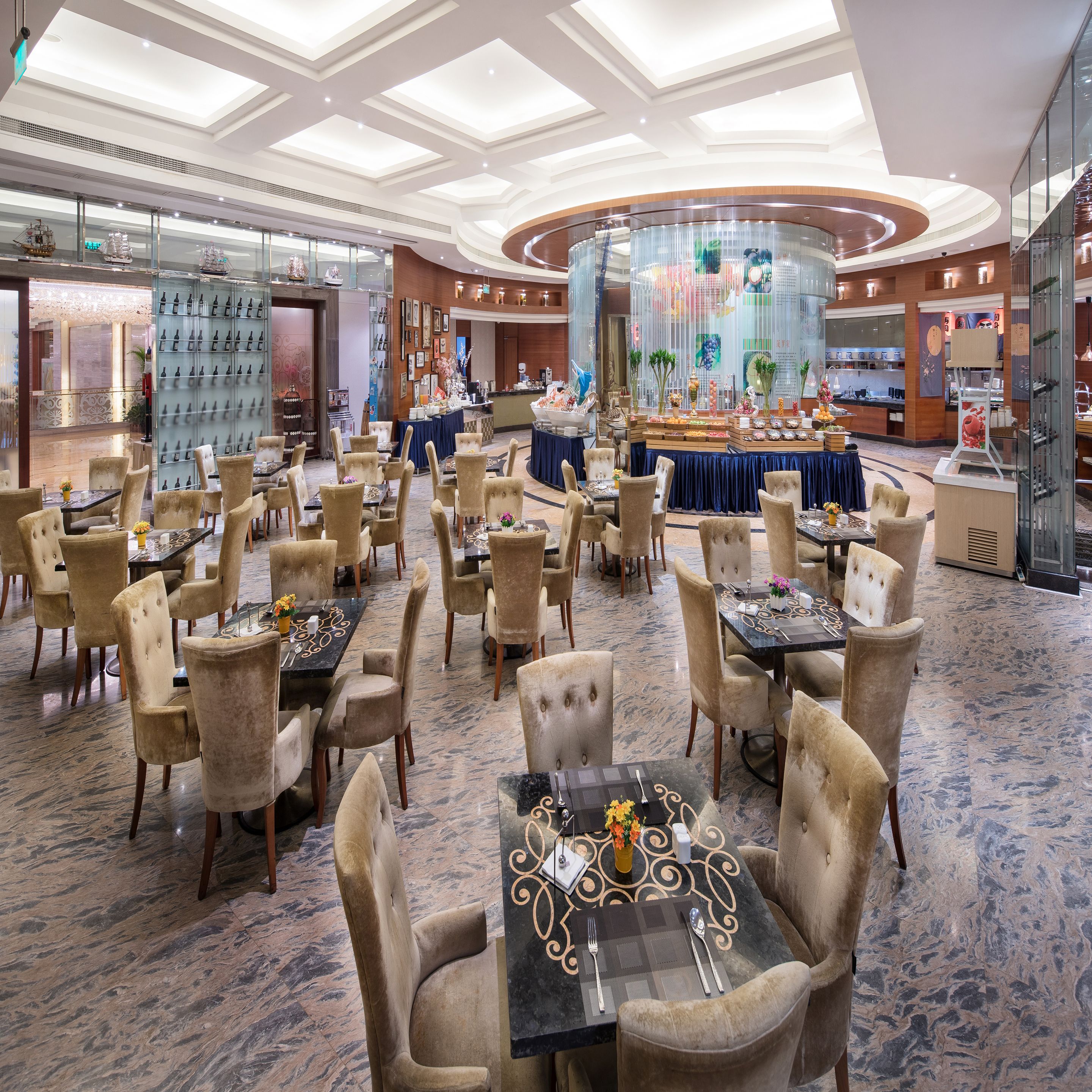 Un vestíbulo de hotel espacioso con varias zonas de restauración, un bar central y una gran exhibición de objetos decorativos.