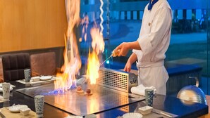 A chef cooking on an open flame grill with a view of a building and trees in the background. - Cinese Hotel Dongguan Shijie (Dongguan)
