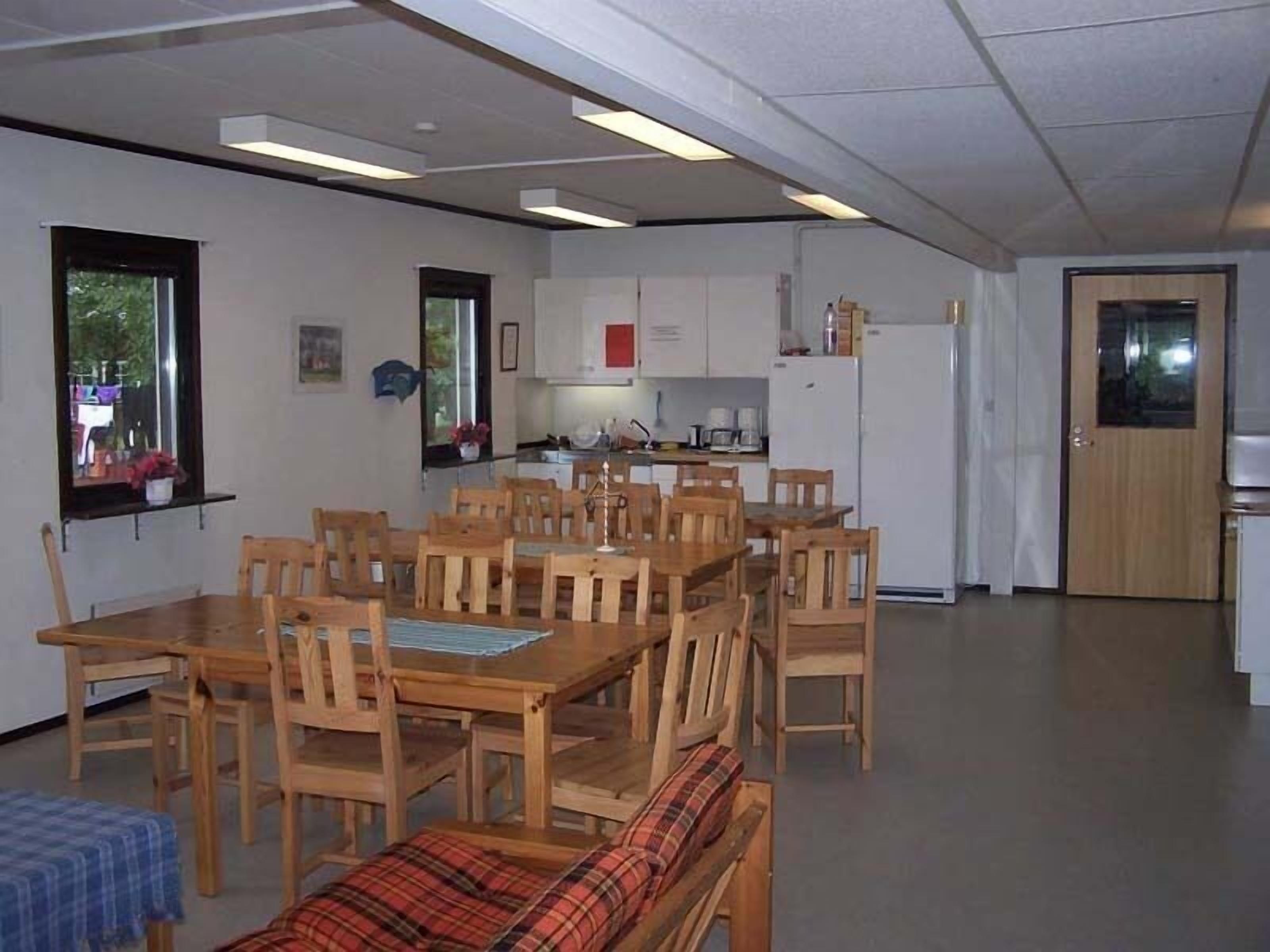 A compact kitchen with white cabinets, a refrigerator, and a dining area with wooden tables and chairs.