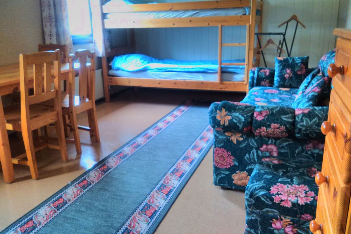 Et værelse med køjeseng, et træskrivebord, en blomstret sofa og et mønstret tæppe.
