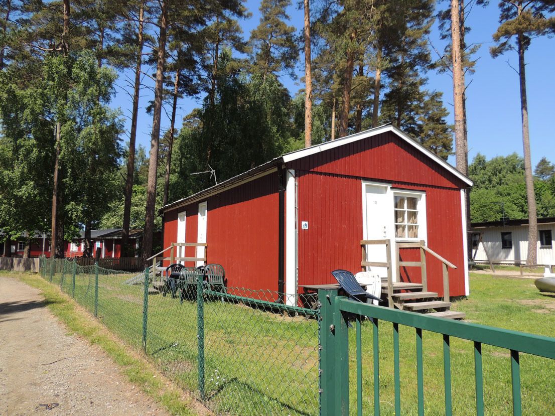A red building with a white door and window, surrounded by a green fence.