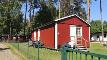 A red building with a white door and window, surrounded by a green fence.
