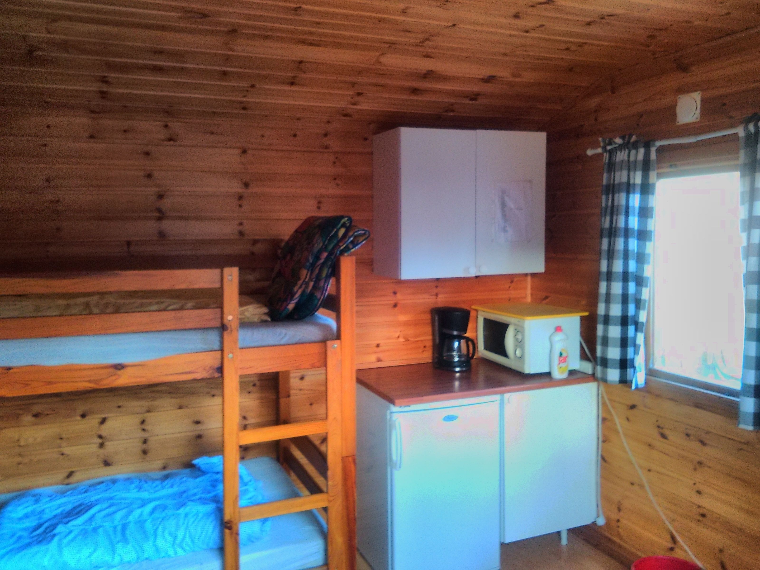 A bunk bed with a ladder, a small kitchenette with a microwave, and a window with curtains.
