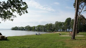 A grassy area with picnic tables and people sitting by a lake.