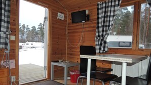 A small cabin with a wooden interior, a table with two chairs, a television mounted on the wall, and a sign indicating the cabin is for rent.