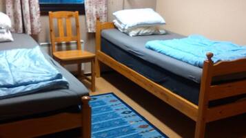 A small, cozy room with two wooden beds, a chair, and a window with curtains.