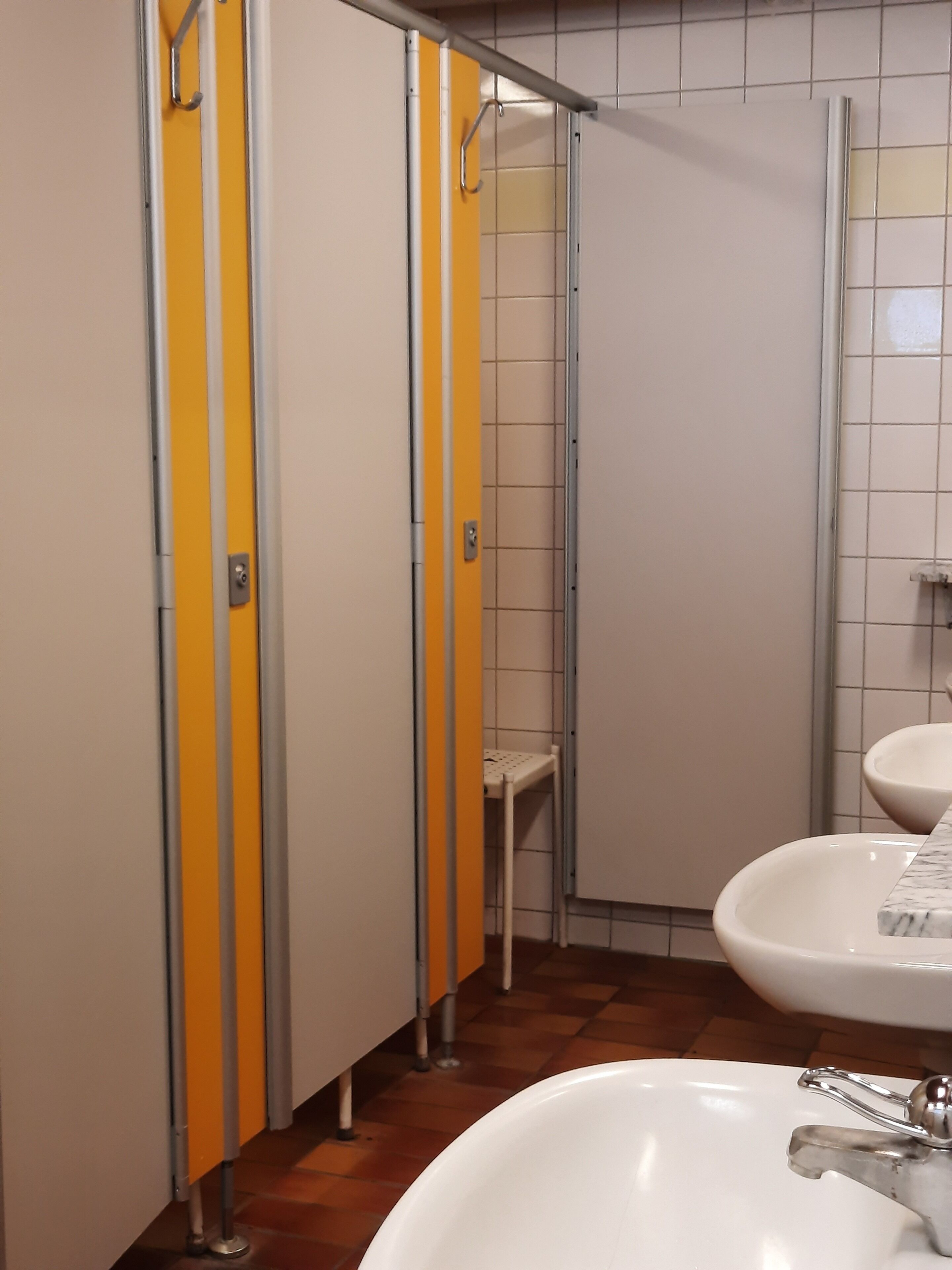 Baño con separadores amarillos y blancos, un lavabo blanco y piso de baldosas.