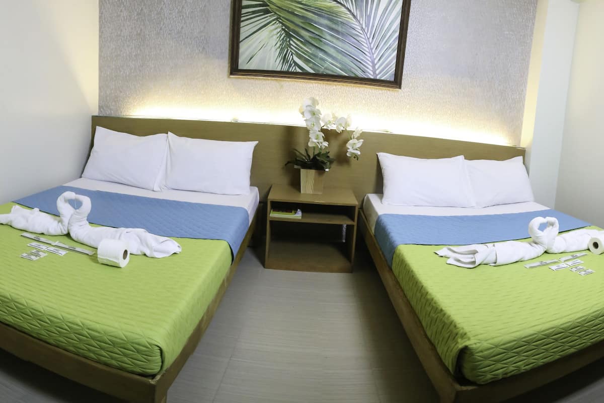 Ein Hotelzimmer mit zwei Betten, beide mit grüner Bettdecke und weißen Kissen. Auf den Betten liegen Handtücher, und dazwischen steht ein kleiner Tisch mit einem Blumenstrauß.