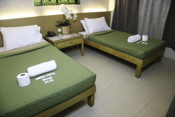 Habitación de hotel con dos camas, cada una con ropa de cama verde, una mesita de noche con un teléfono y una planta, y una ventana con cortinas.