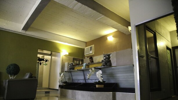 A reception area with a reception desk, a sofa, and a plant. There is a door leading to another room and an air conditioning unit on the wall. - Quoalla Hotel Makati (Makati)