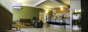 A spacious living area with a sofa, a coffee table, and a small table. There is a reception desk with a counter and a decorative plant. - Quoalla Hotel Makati (Makati)