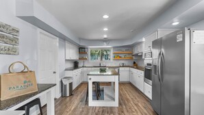 A modern kitchen with white cabinets, a stainless steel refrigerator, and a wooden floor. - Lagerheads (Panama City Beach)