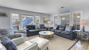 A modern living room with two black leather sofas, a white armchair, and a coffee table. There are large windows with a view of a blue staircase and a beach sign. - Lagerheads (Panama City Beach)