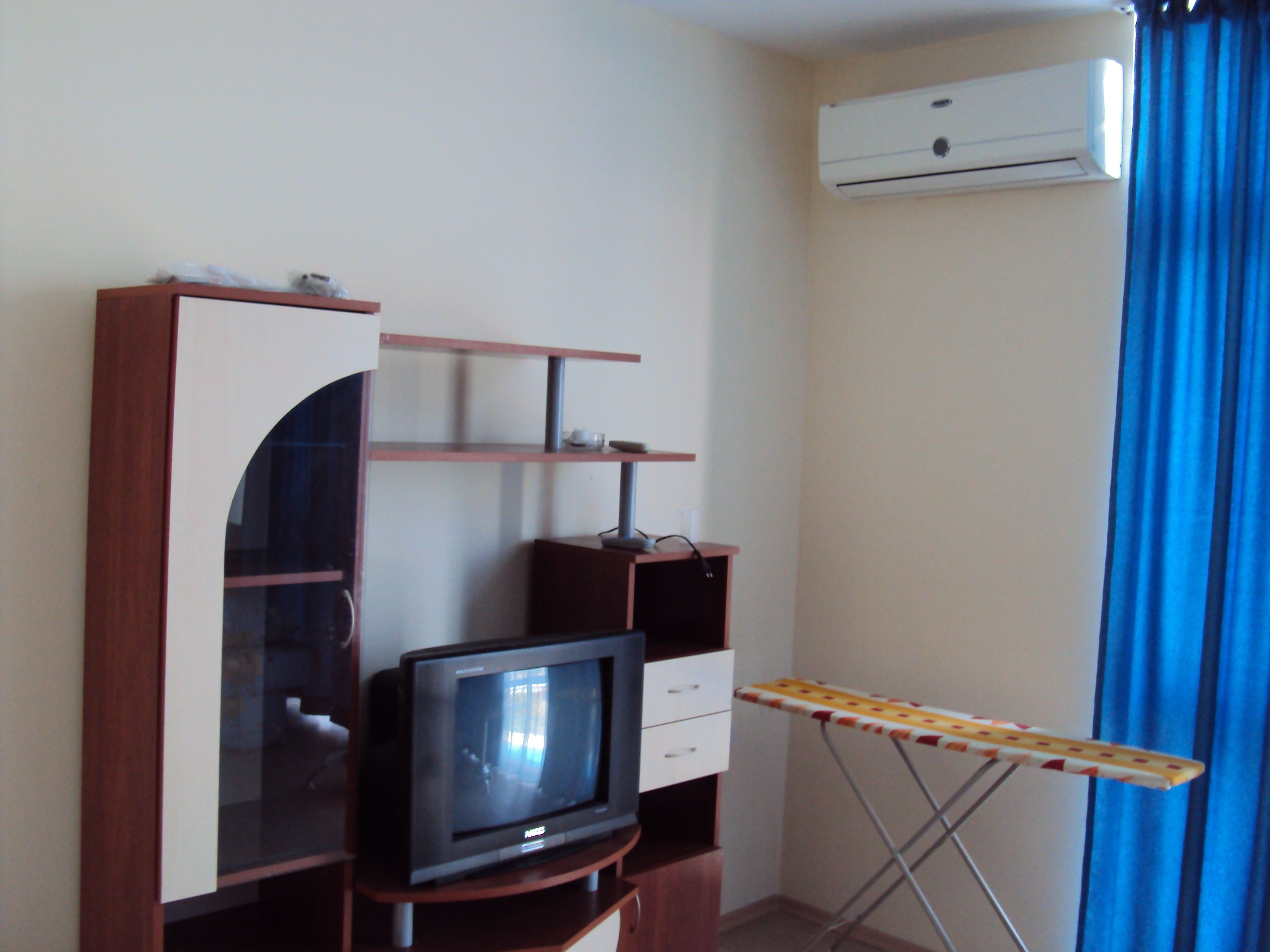 Una habitación con un televisor sobre un soporte de madera, una plancha pequeña y un aire acondicionado de pared.
