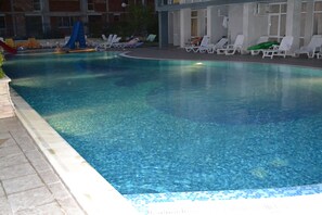 A swimming pool with clear water, surrounded by lounge chairs and a slide.
