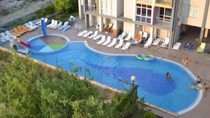 A swimming pool with lounge chairs and a slide, surrounded by a fence and greenery. - Sun City Apartments (Sunny Beach)