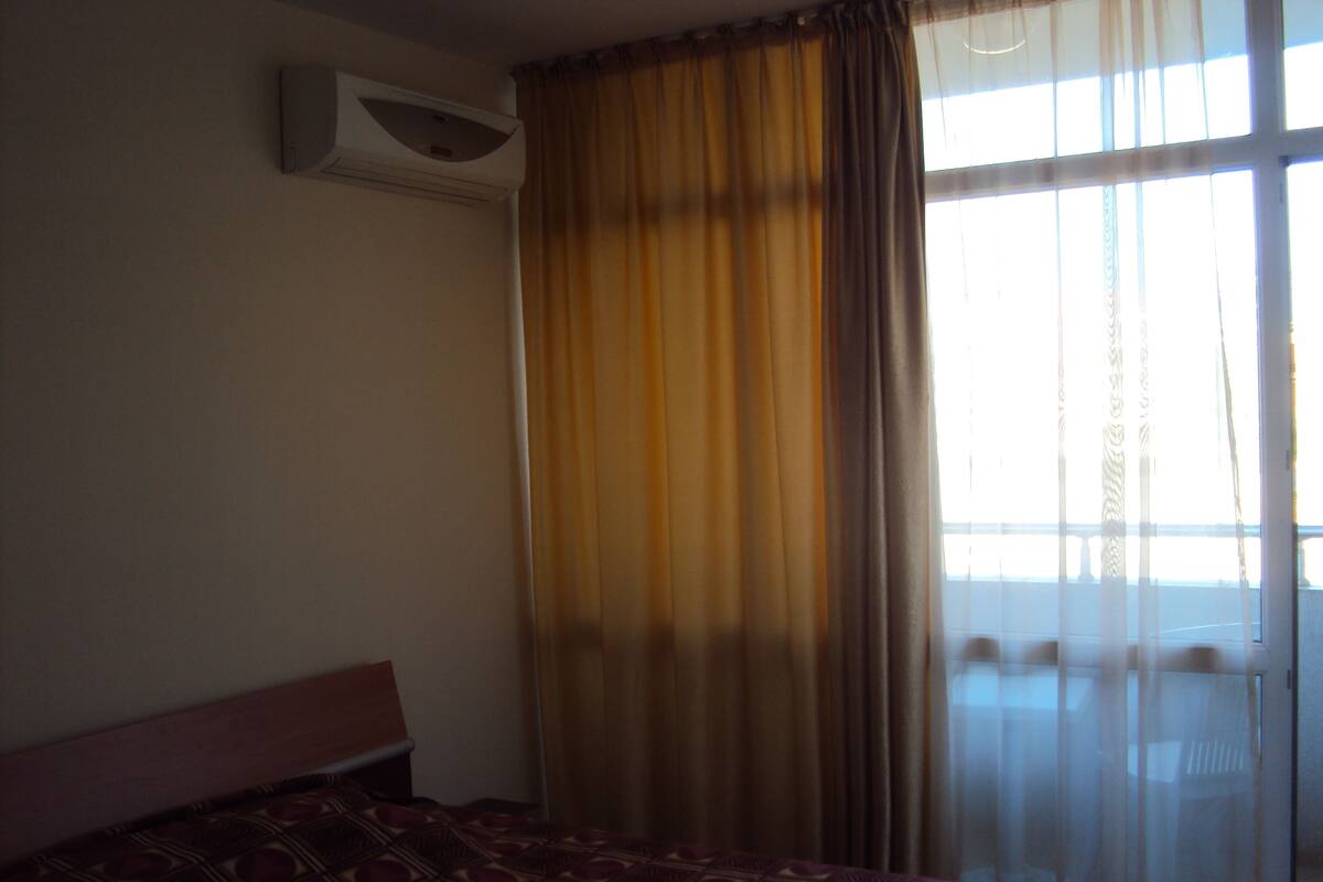 A hotel room with a bed, a window with curtains, and an air conditioning unit on the wall.
