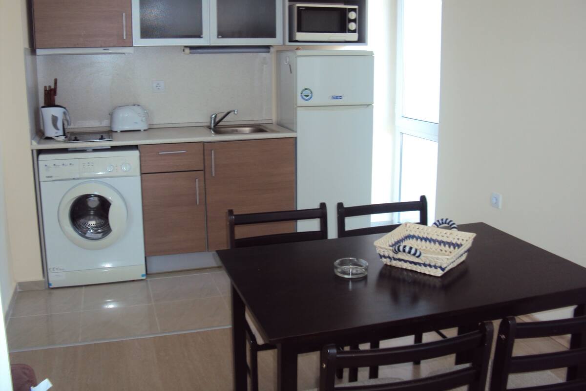 A compact kitchen with a washing machine, microwave, and a dining area with a table and chairs.