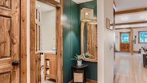 A hallway with wooden doors, a green wall, a small table with a plant, and a hanging lamp.