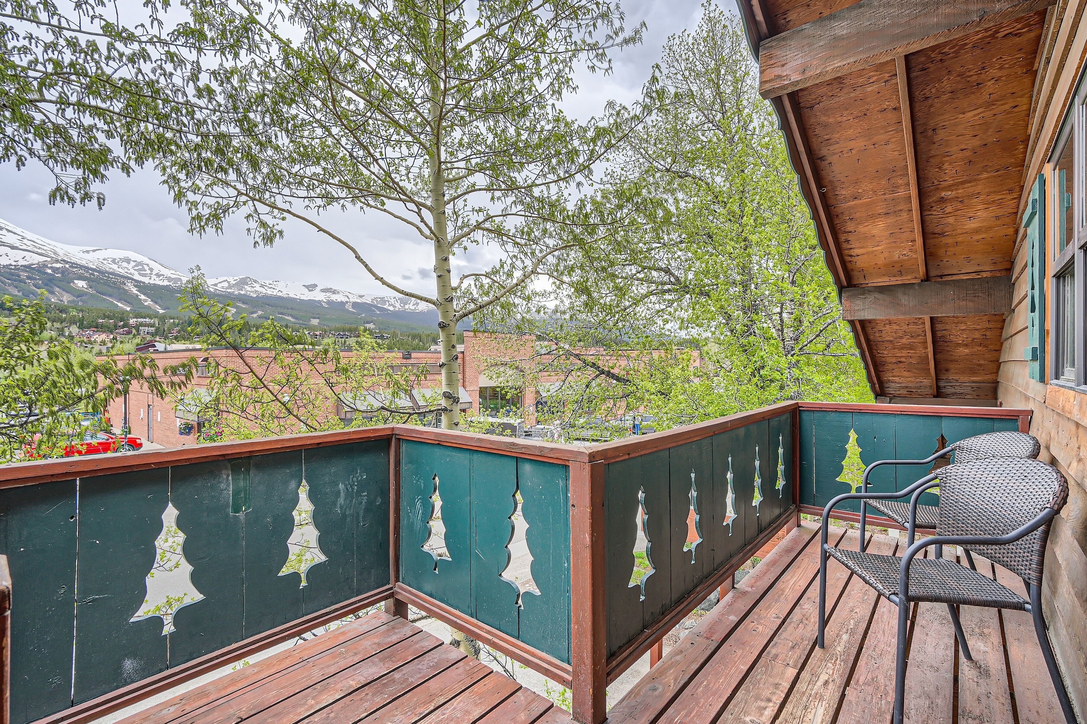 Une terrasse en bois offrant une vue sur des montagnes enneigées et un arbre.