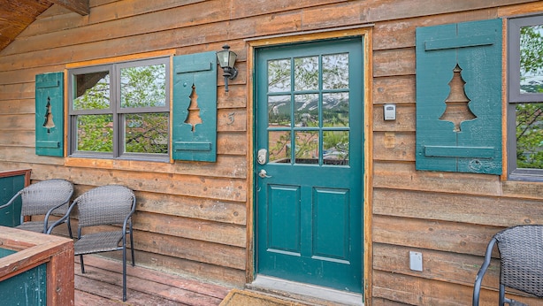 A wooden cabin with a green door, shutters, and a porch with wicker chairs.