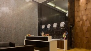 A modern reception area with a black and white checkered floor, a black sofa, and a white reception desk. - Iris Premire (Ahmednagar)