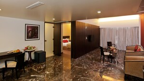 A hotel room with a marble floor, a dining area with a table and chairs, a sofa, and a bed with a red pillow. - Iris Premire (Ahmednagar)