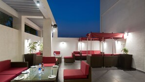 An outdoor patio with wicker furniture, red cushions, and glass-top tables. - Iris Premire (Ahmednagar)