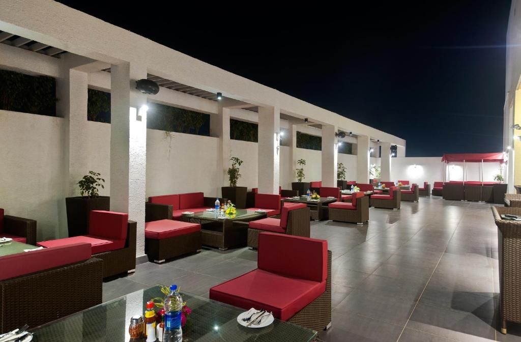An outdoor seating area with red cushioned chairs and tables, surrounded by a white wall with windows.