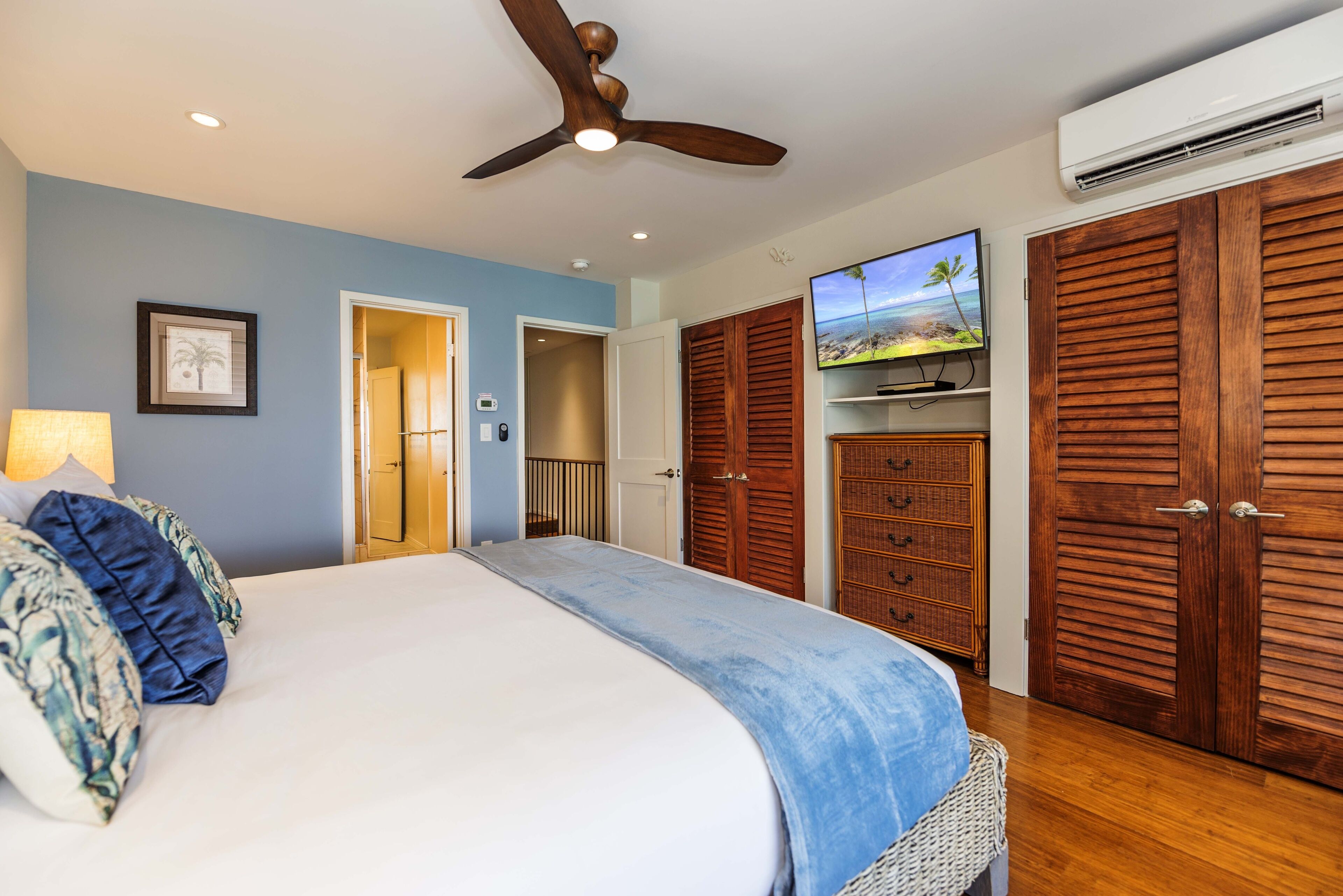 A bedroom with a bed, a ceiling fan, a TV, and wooden wardrobes.