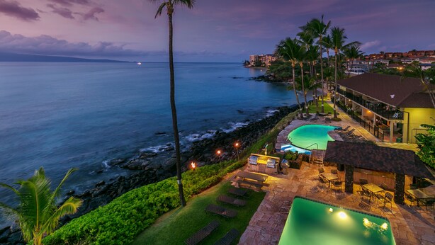 Un complexe hôtelier doté d’une piscine, de chaises longues et offrant une vue sur l’océan au crépuscule.
