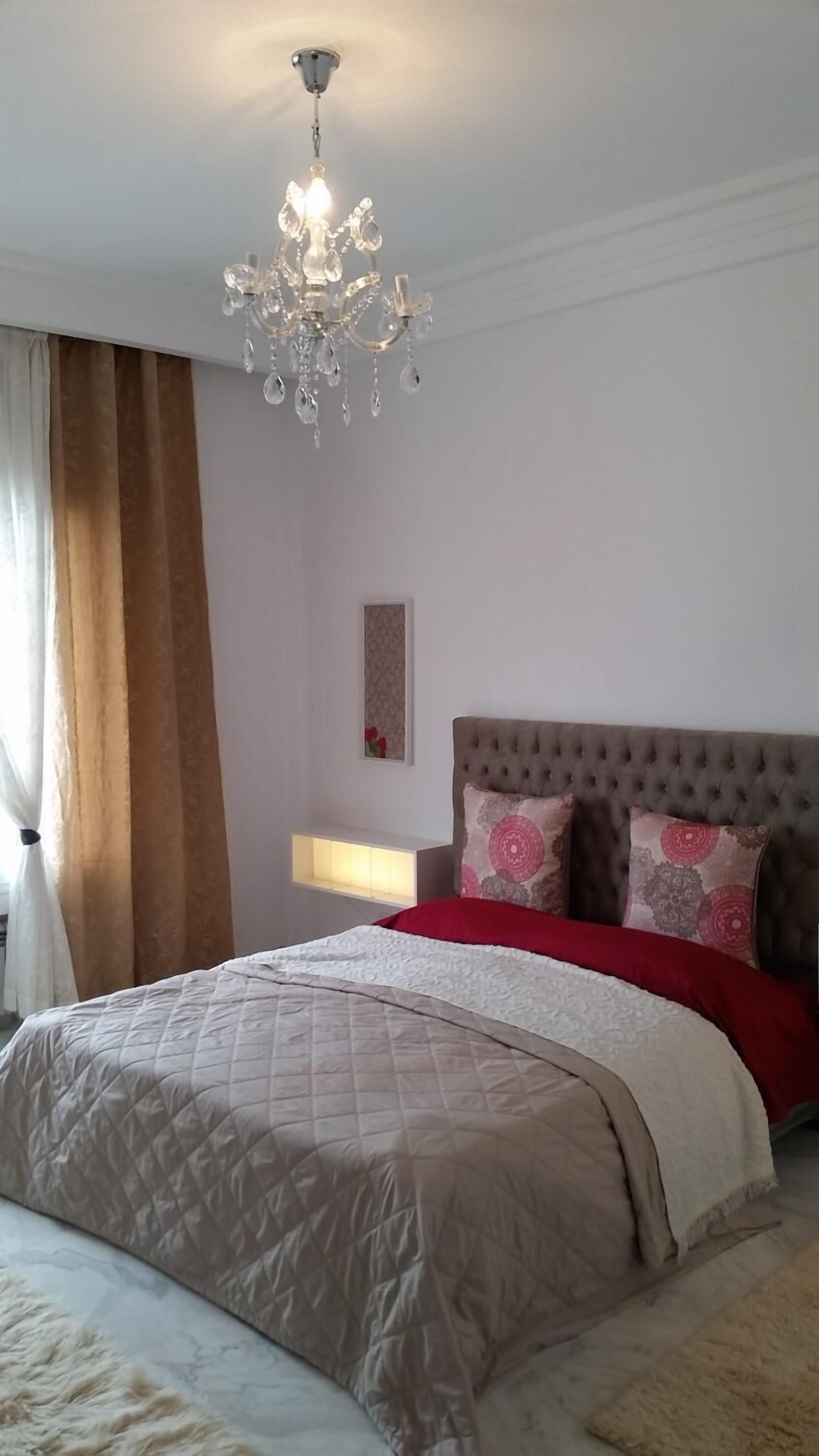 Une chambre à coucher avec un grand lit, un lustre, une table de chevet et une lampe fixée au mur.