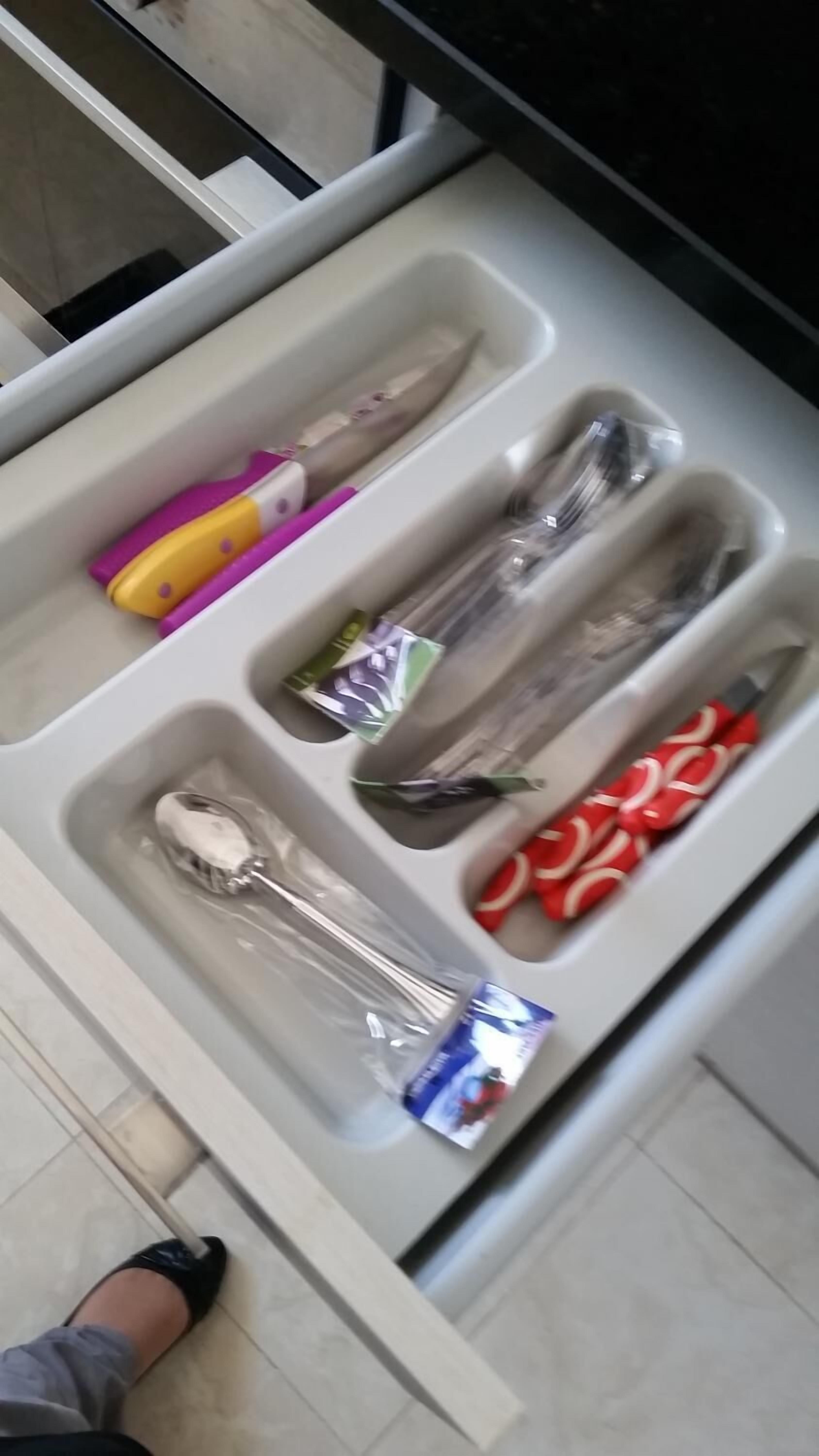A drawer with compartments containing various items including a plastic bag, a pair of scissors, a packet of tissues, and a red patterned item.