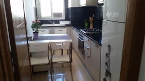 A compact kitchen with a dining area, a refrigerator, a sink, and a window. - Appartement Haut Standing Lac 2 (Tunis)