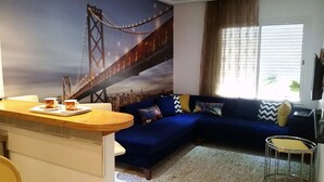 A living room with a blue sofa, a coffee table, and a mural of a bridge. - Appartement Haut Standing Lac 2 (Tunis)